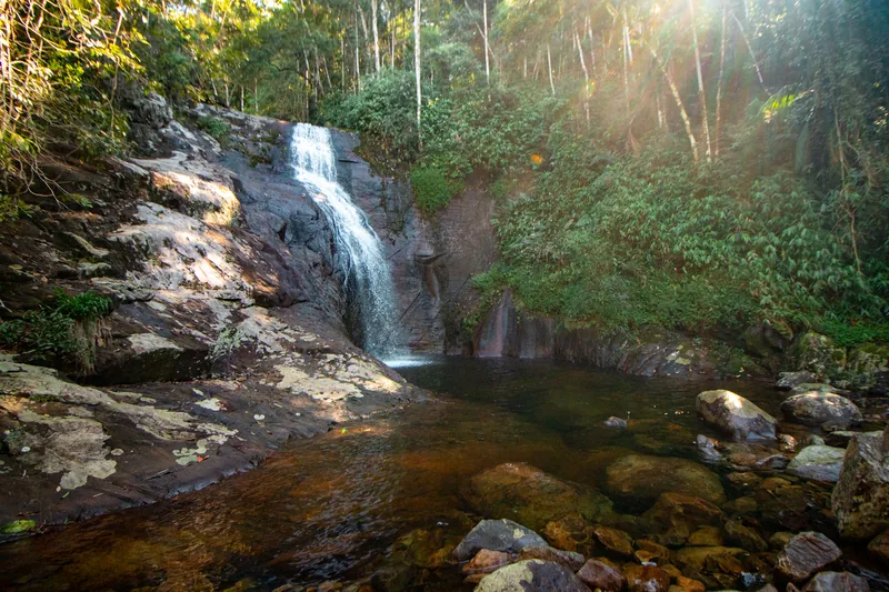 Cachoeira caindo sobre paredão de pedra em meio à mata do Caparaó